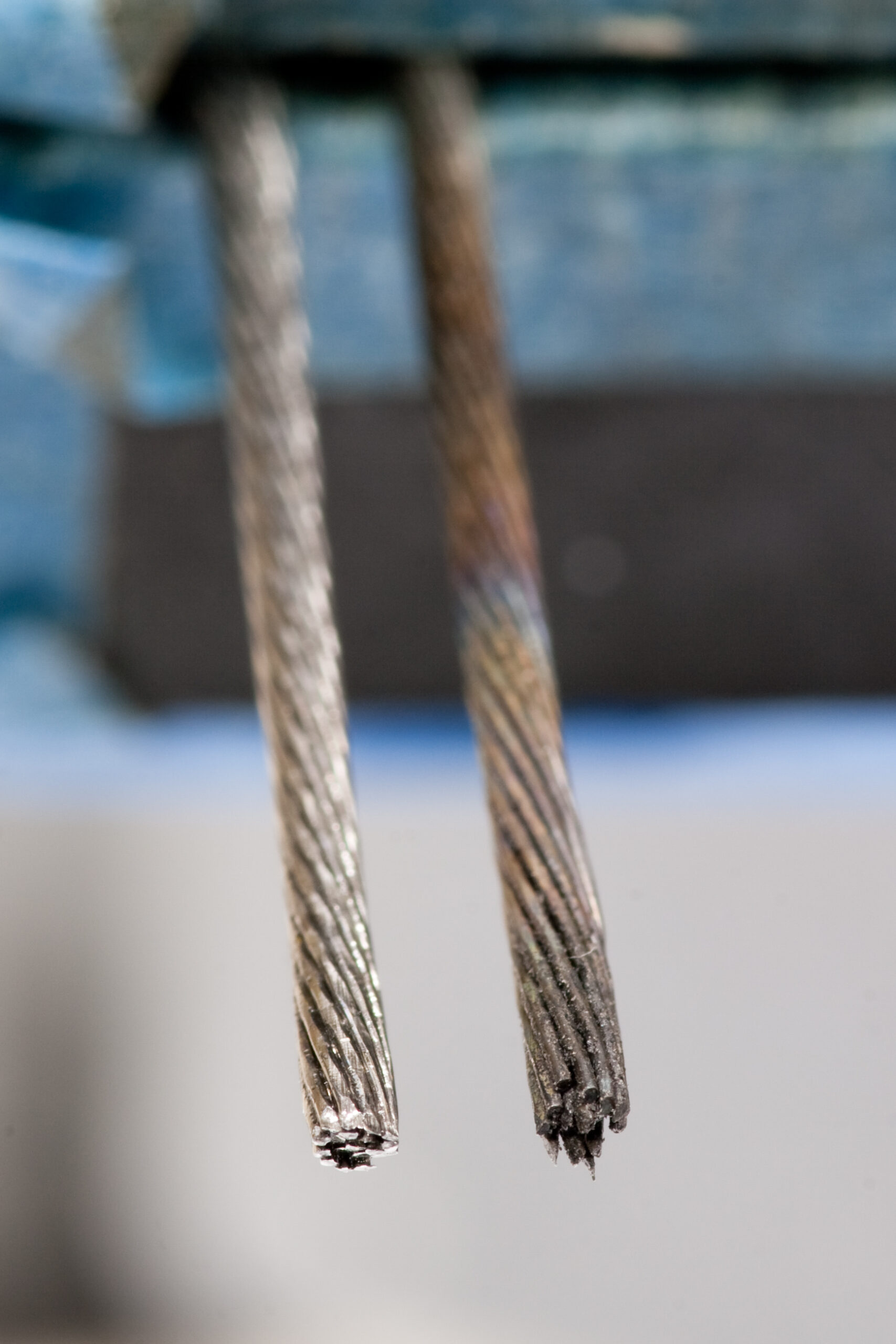 Two pieces of cut bicycle cable. The piece on the left was stuck together with cyanoacrylate glue, the piece on the right was an attempt at soldering with an iron and torch.