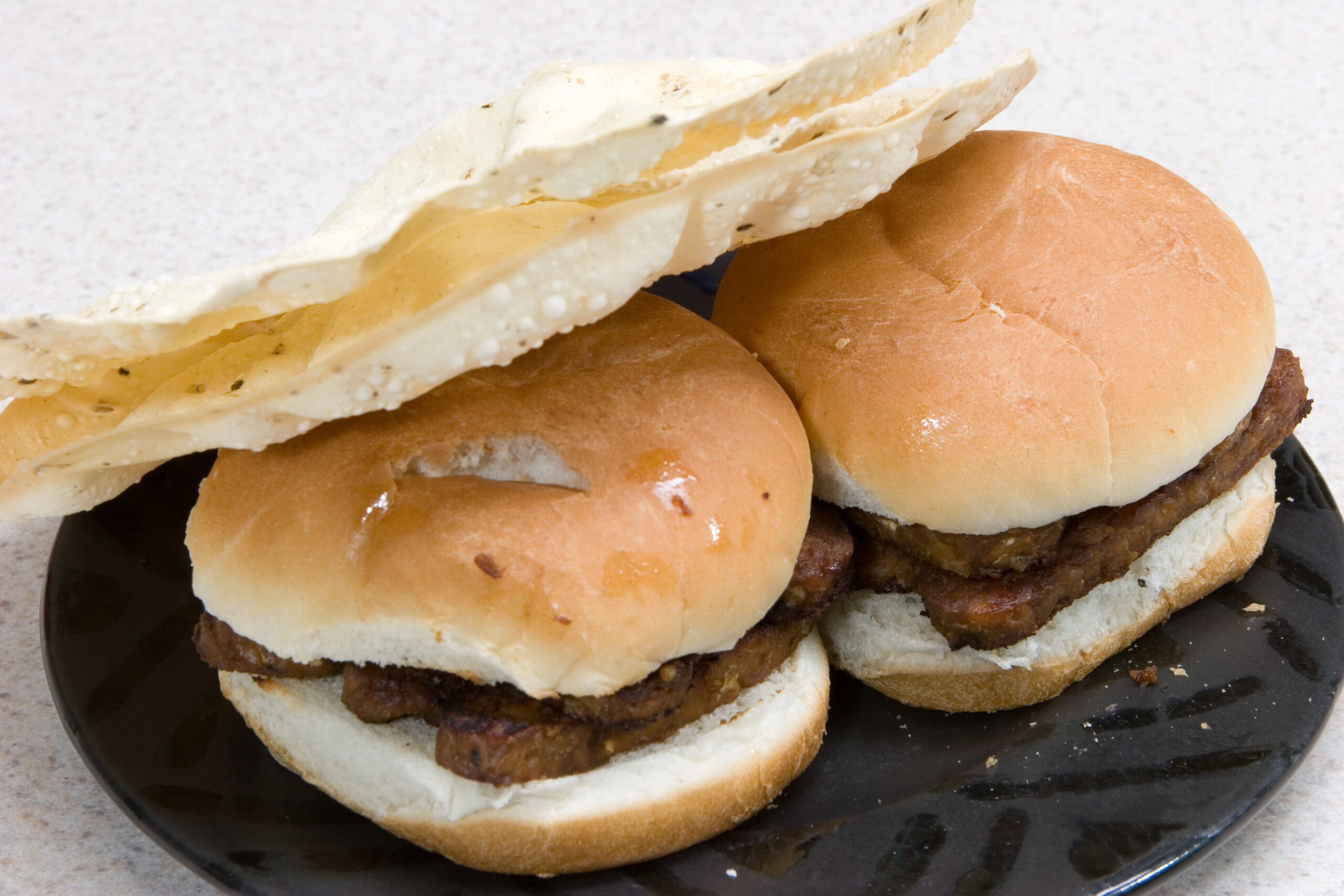 Tempeh marinated in teryaki sauce, tahini, and roasted garlic then grilled in a bit of oil and served on a bun. Two papadoms are used as a side dish.