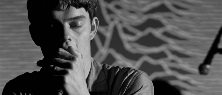 Screen capture from Control of Sam Riley as Ian Curtis, with the Unknown Pleasures album artwork in the background.